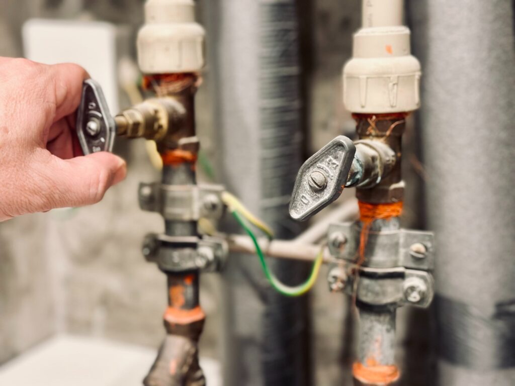 Man using strength to turn a water valve on a pipe gripping it with his hand indoors in a utility room in a close up view