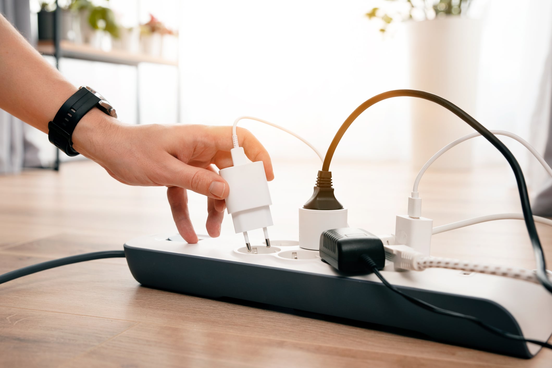 Person is plugging in a device to a power strip. Man holding phone charger.